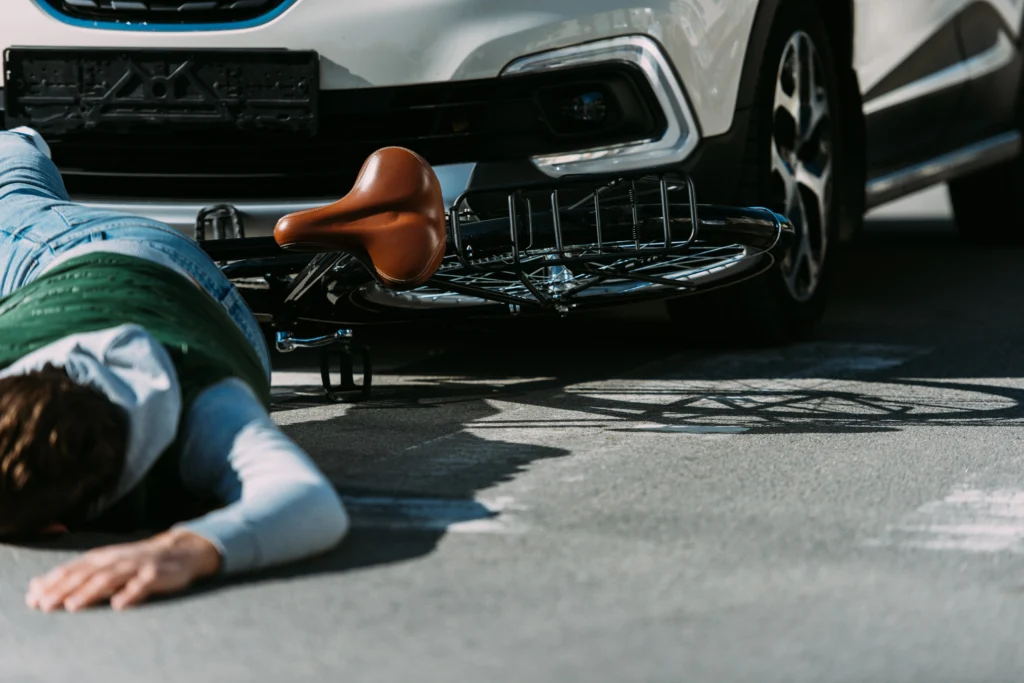 A person lying on the ground next to a bicycle bump by a car.