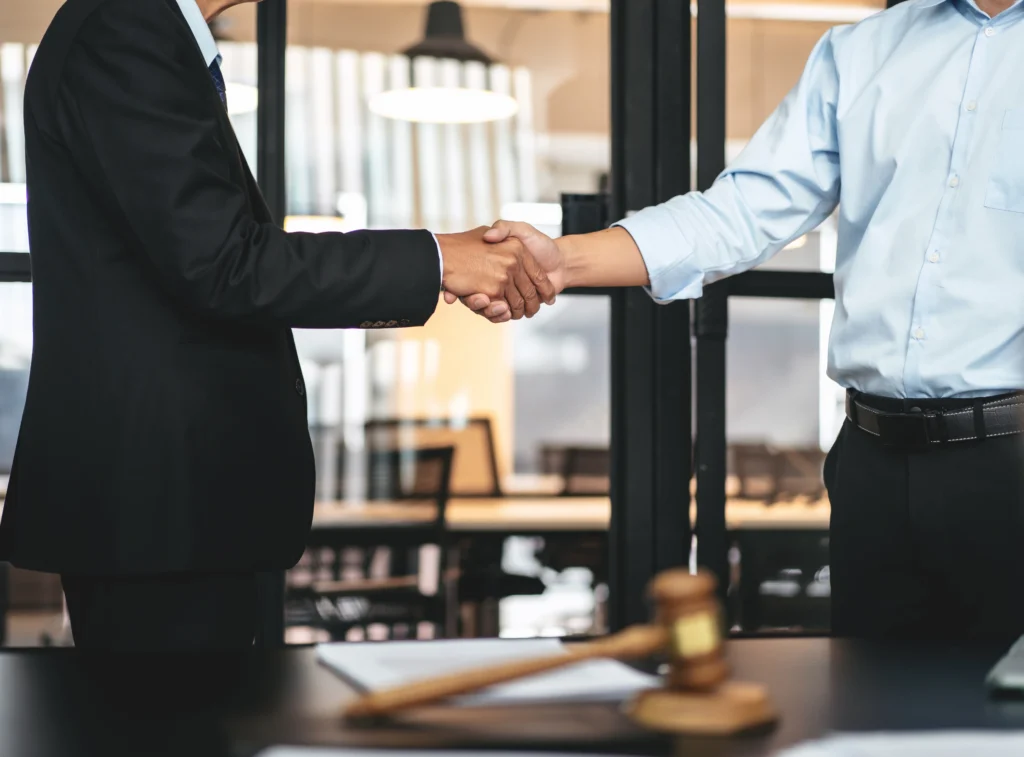 A close-up of a man in a business setting shaking hands, wearing a shirt.